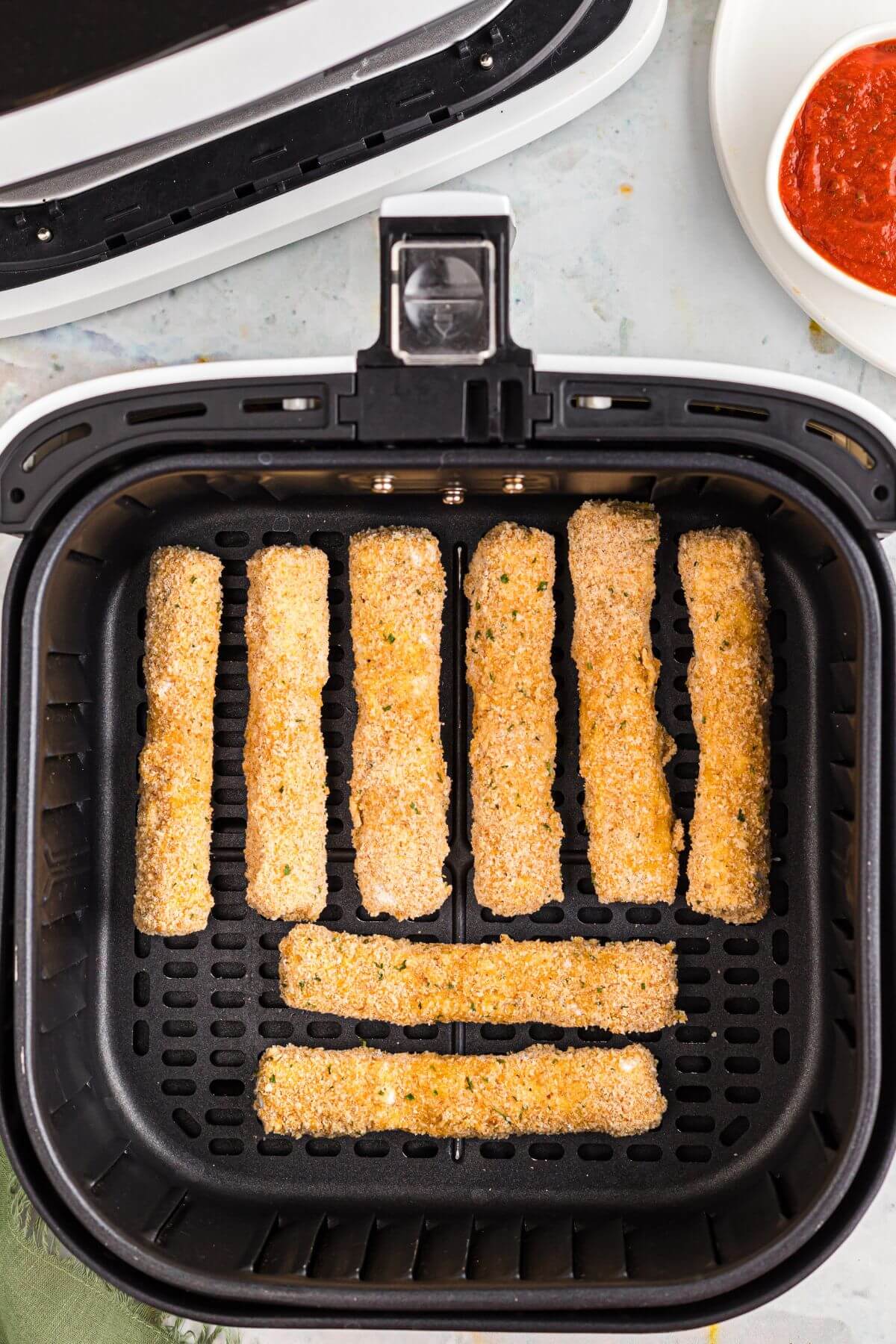 Breaded mozzarella cheese sticks in the air fryer basket before being air fried. 
