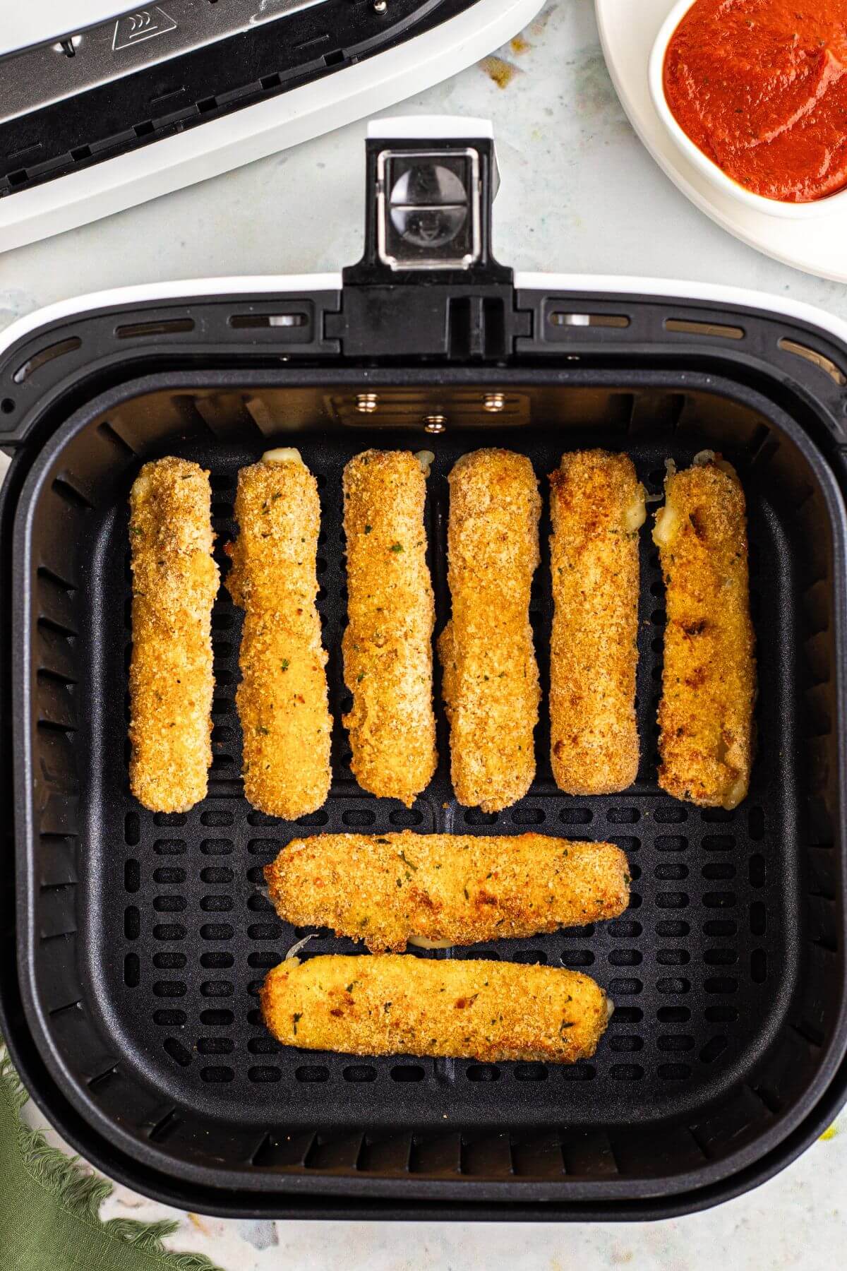 Golden brown breaded mozzarella sticks in the air fryer basket after being air fried. 
