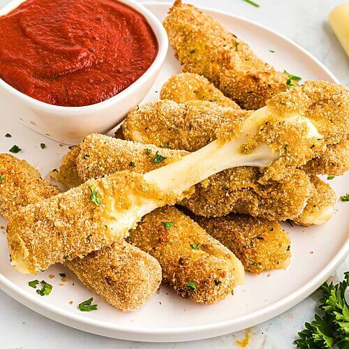 Golden breaded mozzarella cheese sticks stacked on a white plate with marinara sauce.