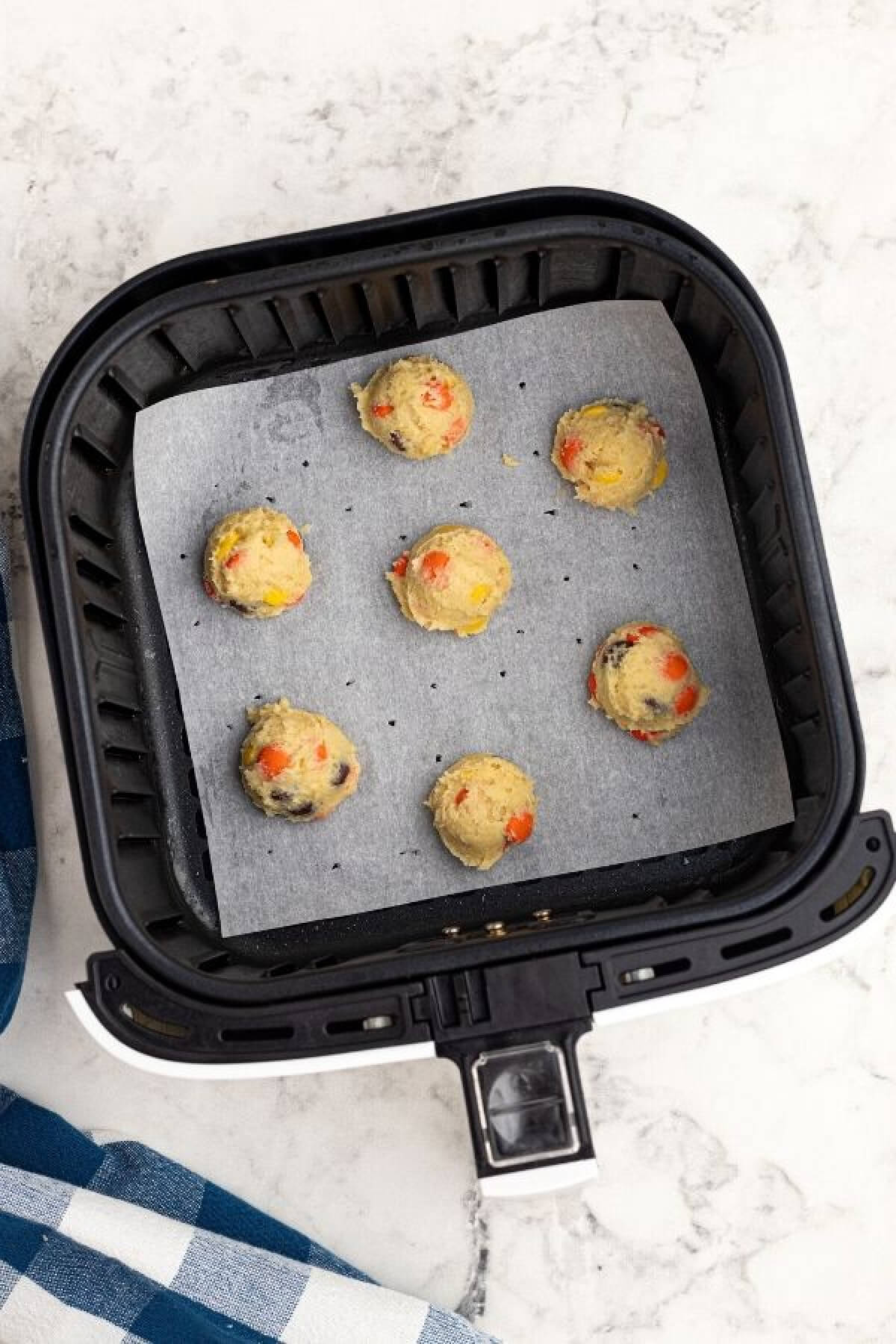 Cookie dough scooped into the air fryer basket onto parchment paper before cooking. 