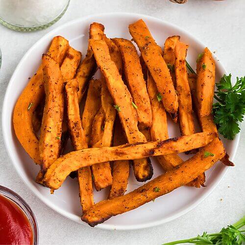 Sweet potato fries on a white round plate with small dish of ketchup.