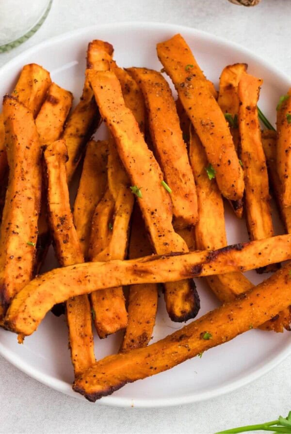 Sweet potato fries on a white round plate with small dish of ketchup.