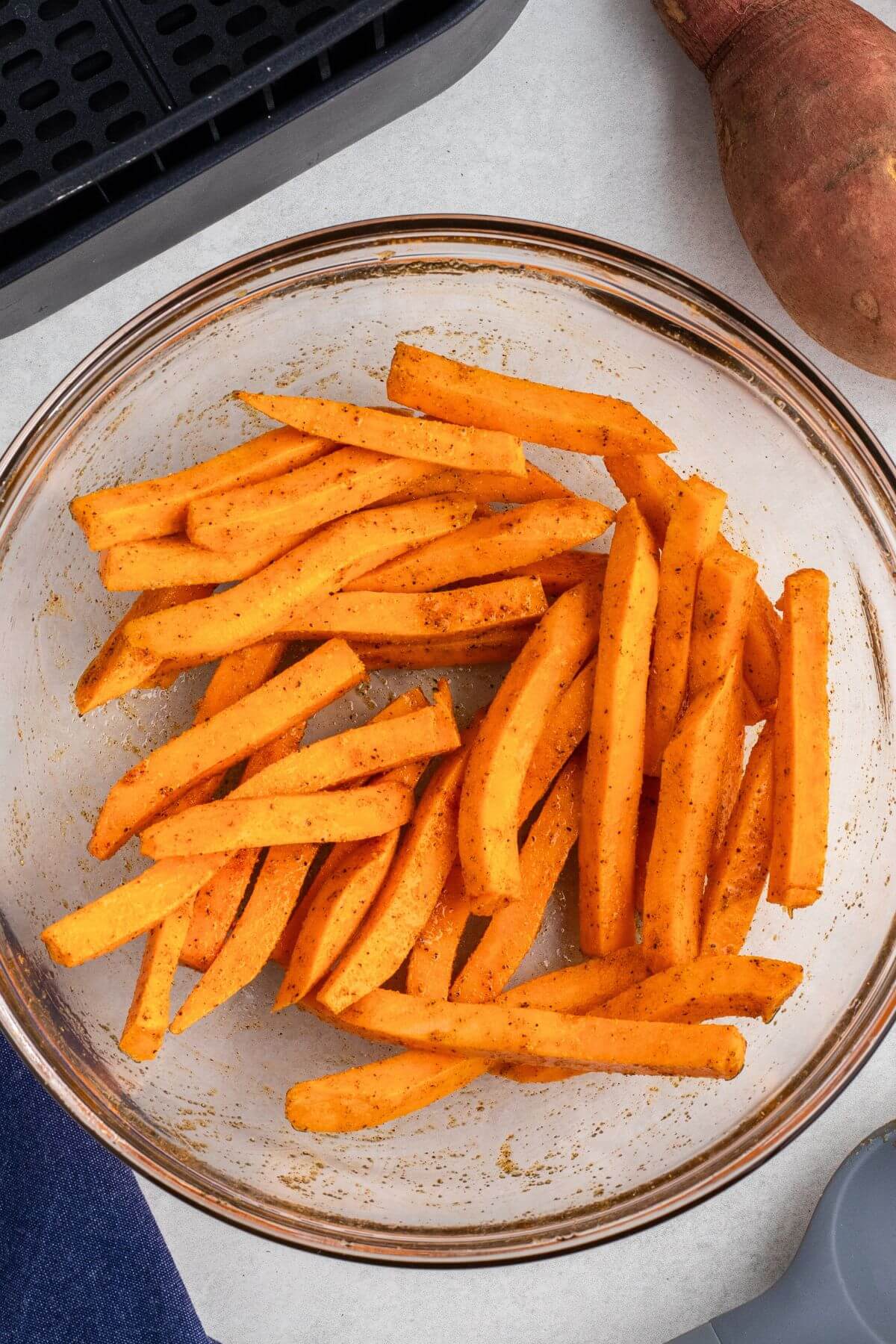 Sweet potatoes cut into strips and tossed with olive oil and seasonings in a clear glass bowl. 