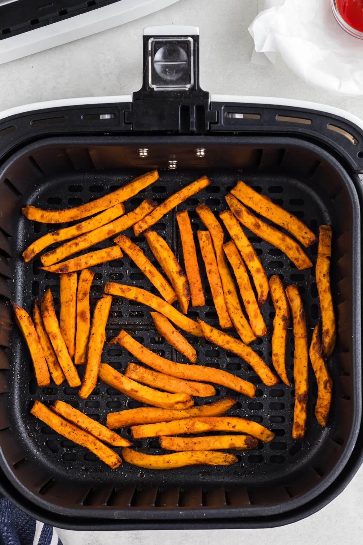 Seasoned sweet potato fries in the air fryer basket after being cooked. 