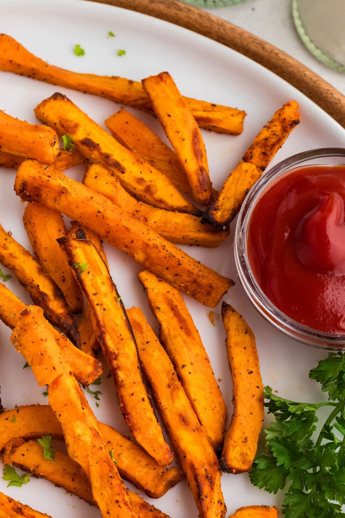 Sweet potato fries on a round white plate with ketchup and parsley.