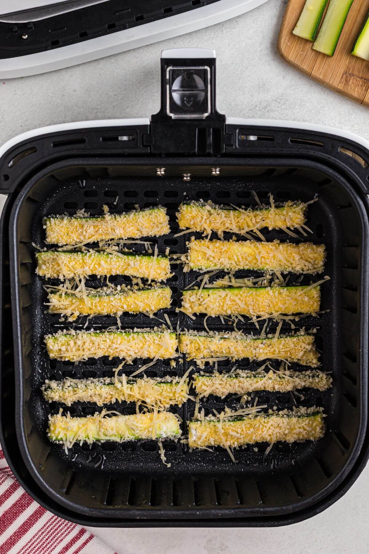 Zucchini sticks breaded and placed in the air fryer basket before being cooked. 
