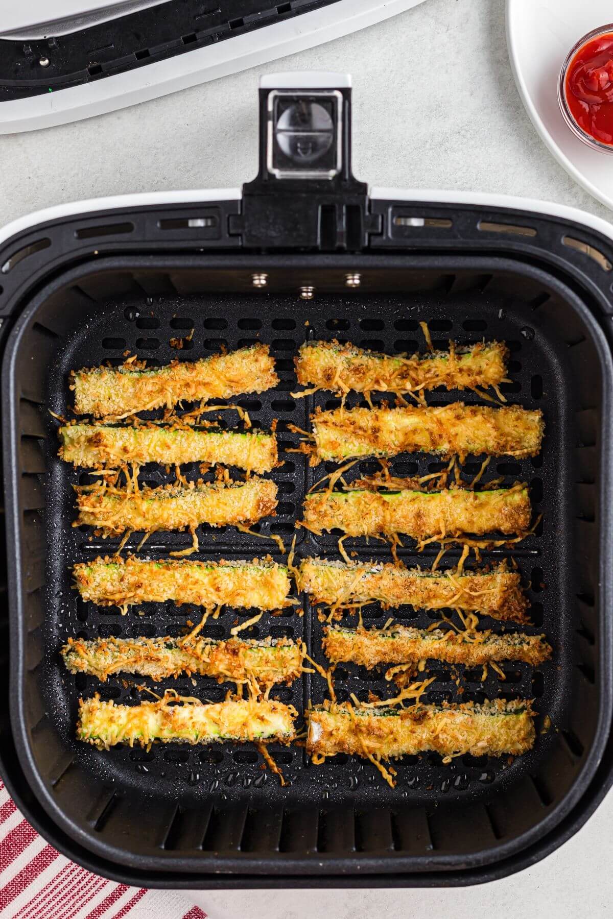 Crispy golden brown cheesy zucchini fries in the air fryer basket after being cooked. 