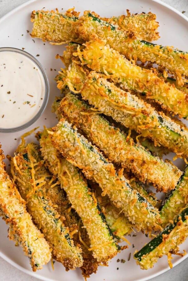 Golden crispy zucchini fries stacked on a white plate.