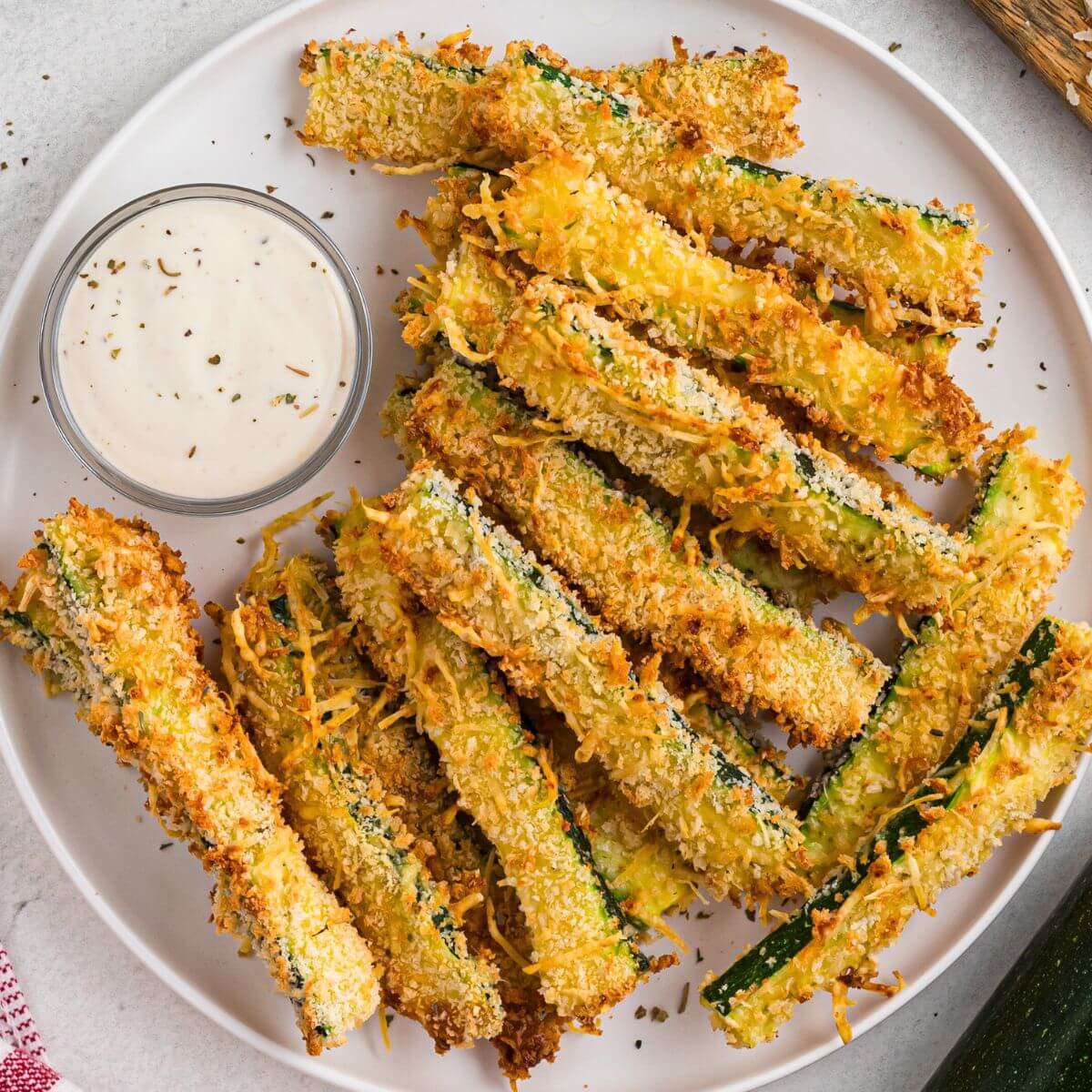 Golden crispy zucchini fries stacked on a white plate.