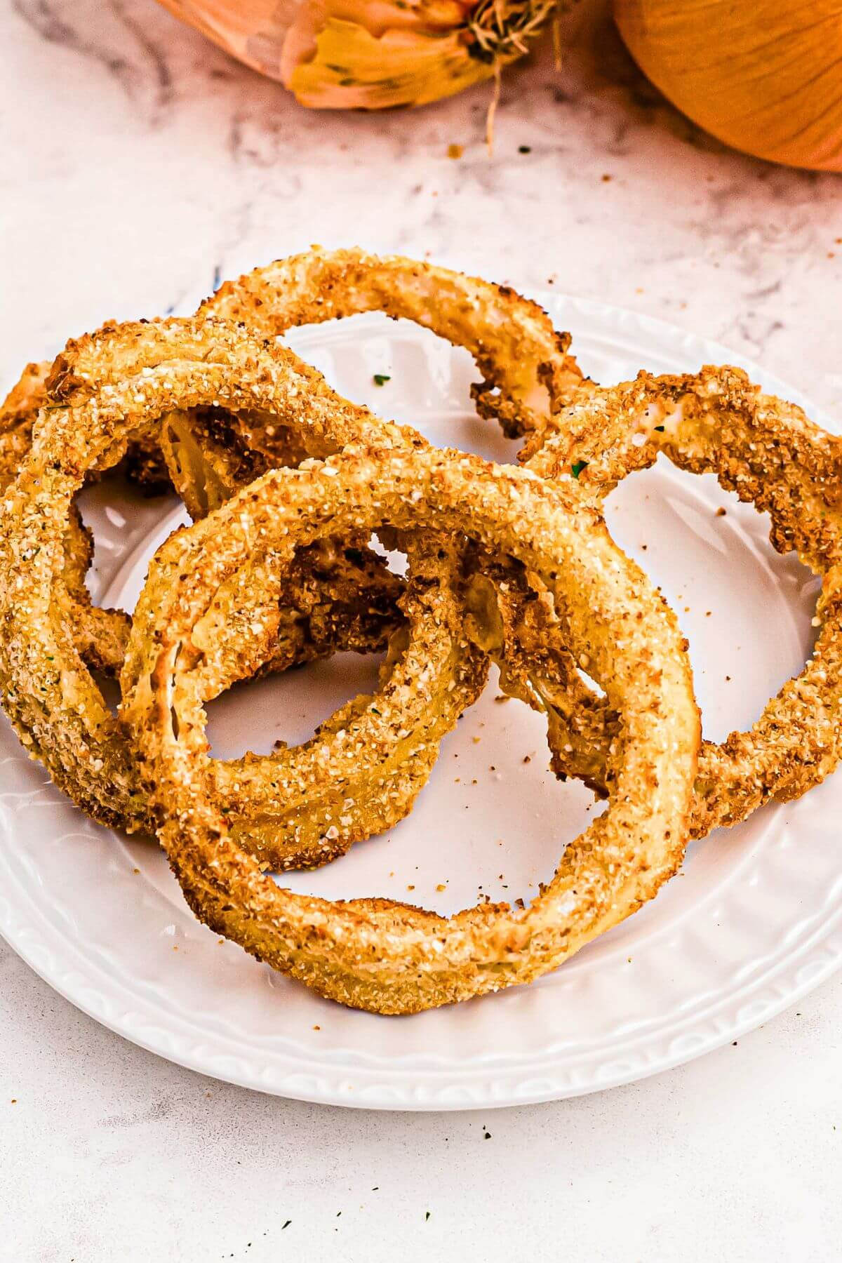 air fryer onion rings stacked on a white plate, ready to eat. 