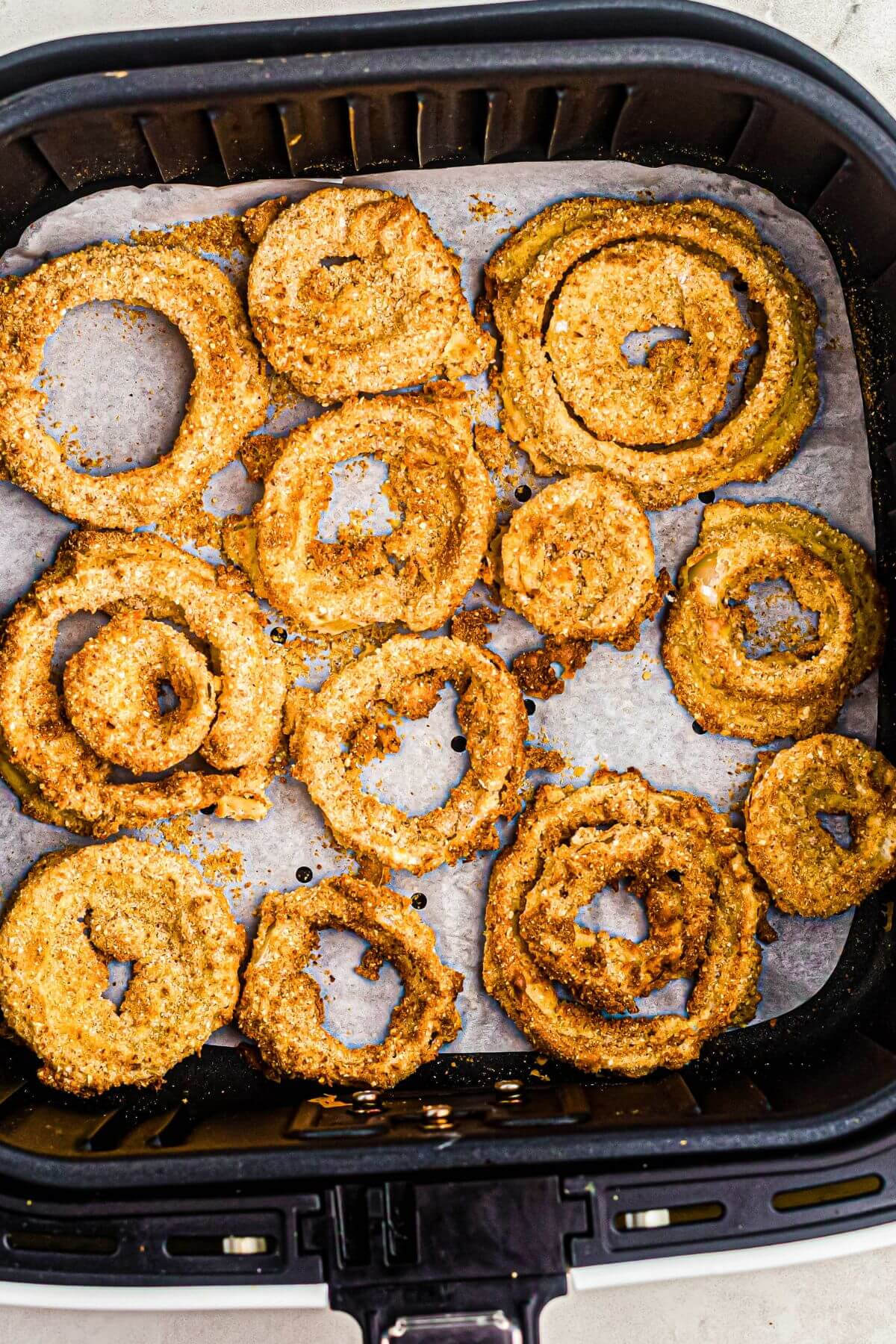 Onion rings being reheated in the air fryer basket on top of a piece of parchment paper that's being used for easier cleanup. 