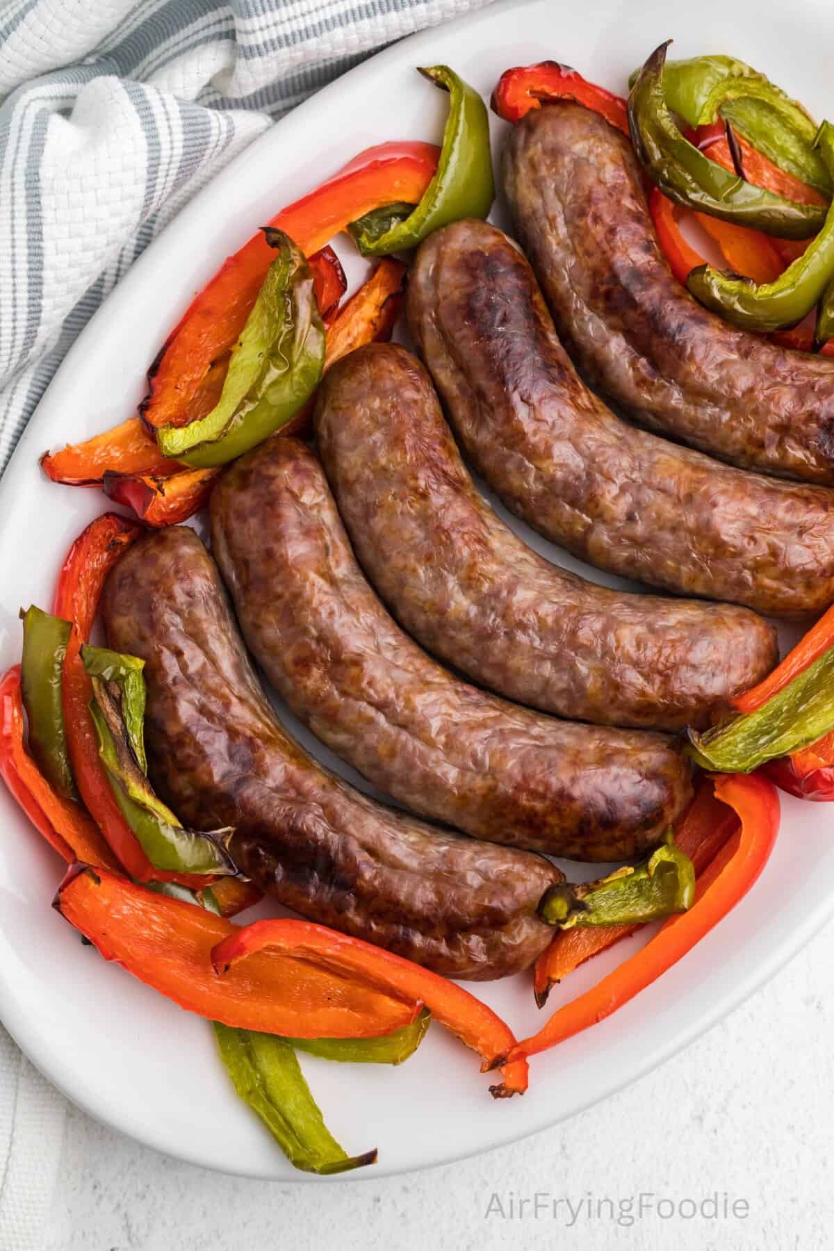 Air fryer brats on a platter with red and green peppers. 
