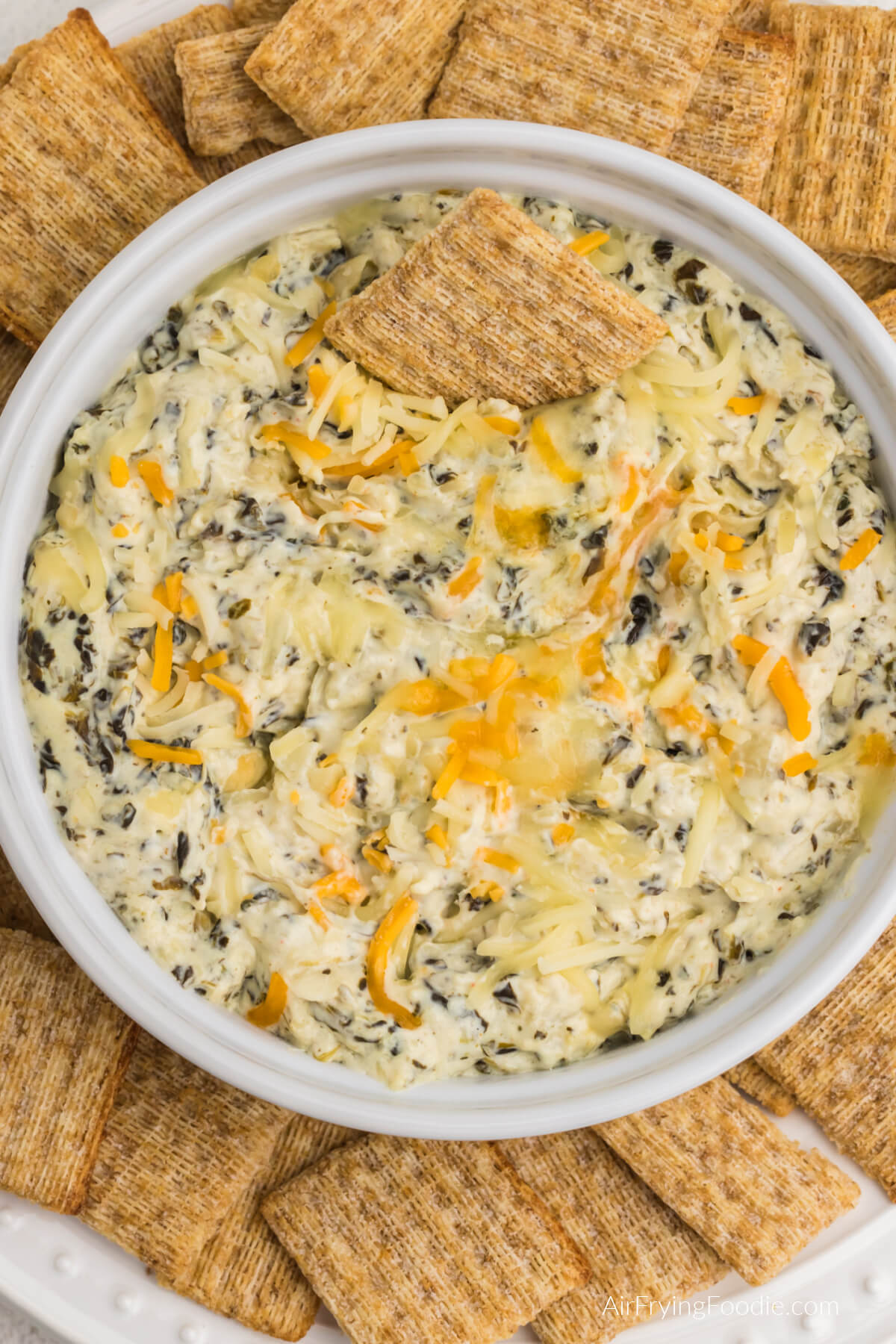 Air fried artichoke spinach dip in a round white dish, surrounded by Triscuit chips for serving. 