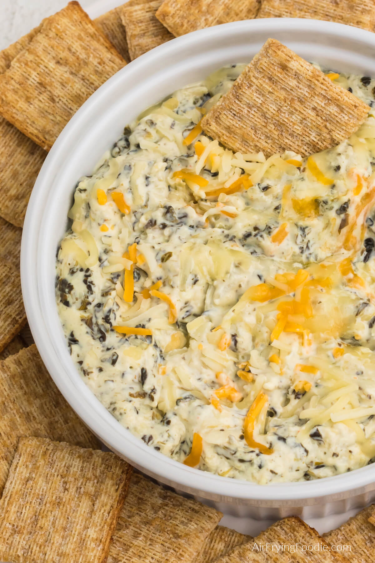 Artichoke spinach dip in an air fryer safe dish, surrounded by Triscuit crackers for dipping. 