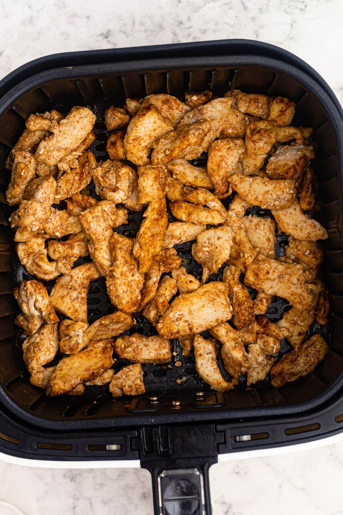 Golden brown seasoned and cooked chicken pieces in the air fryer basket. 