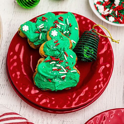 Cinnamon roll Christmas trees frosted with green icing and sprinkles on a red plate.