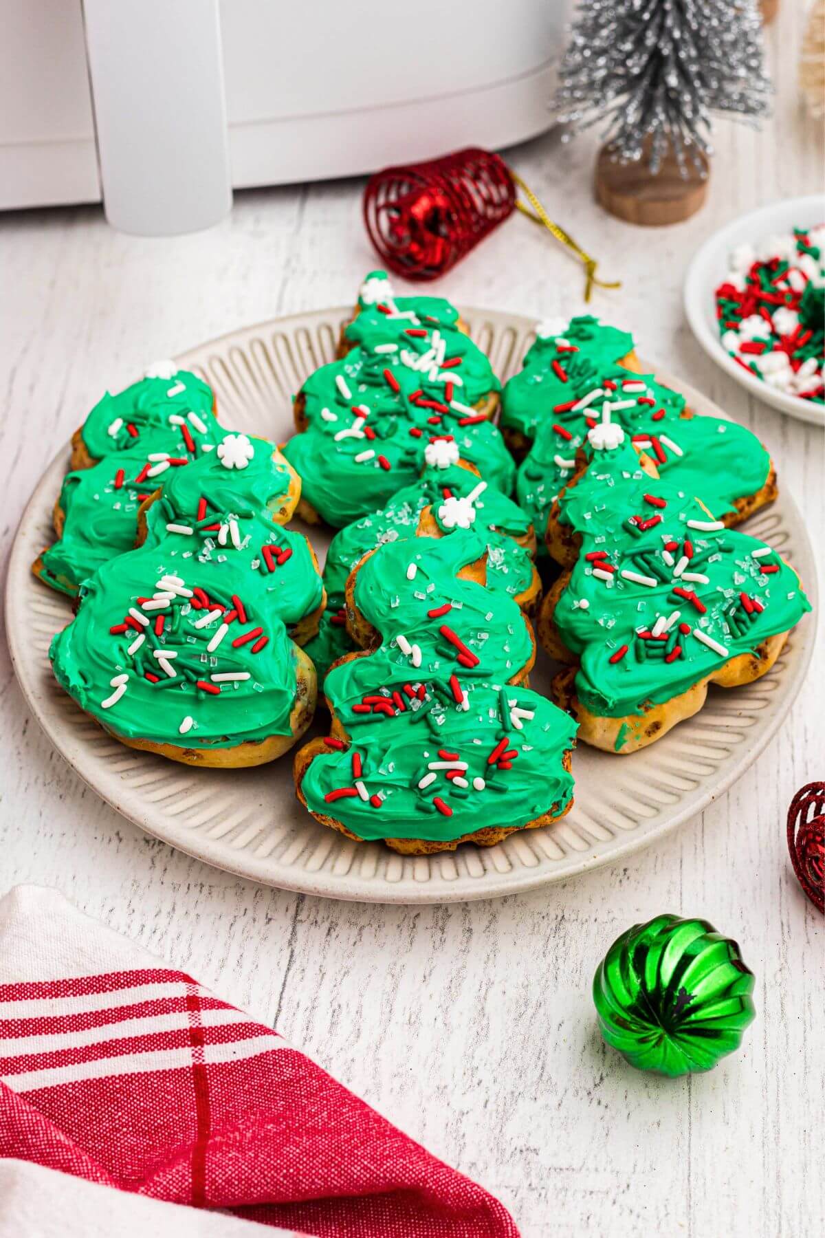 Golden cinnamon rolls frosted with green icing and decorated with holiday sprinkles on a cream plate. 