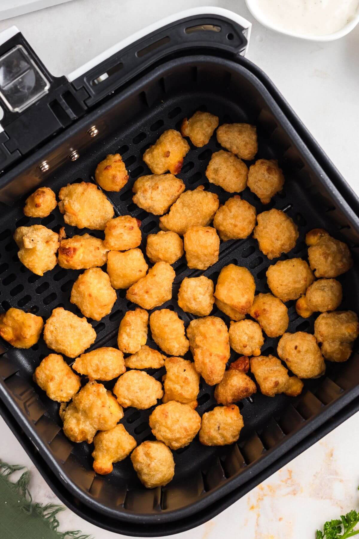 Golden brown breaded cheese curds in the air fryer basket after being cooked. 