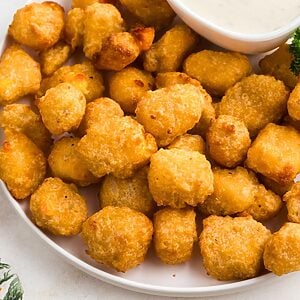 Golden brown breaded cheese curds stacked on a white plate with ranch dressing dip.