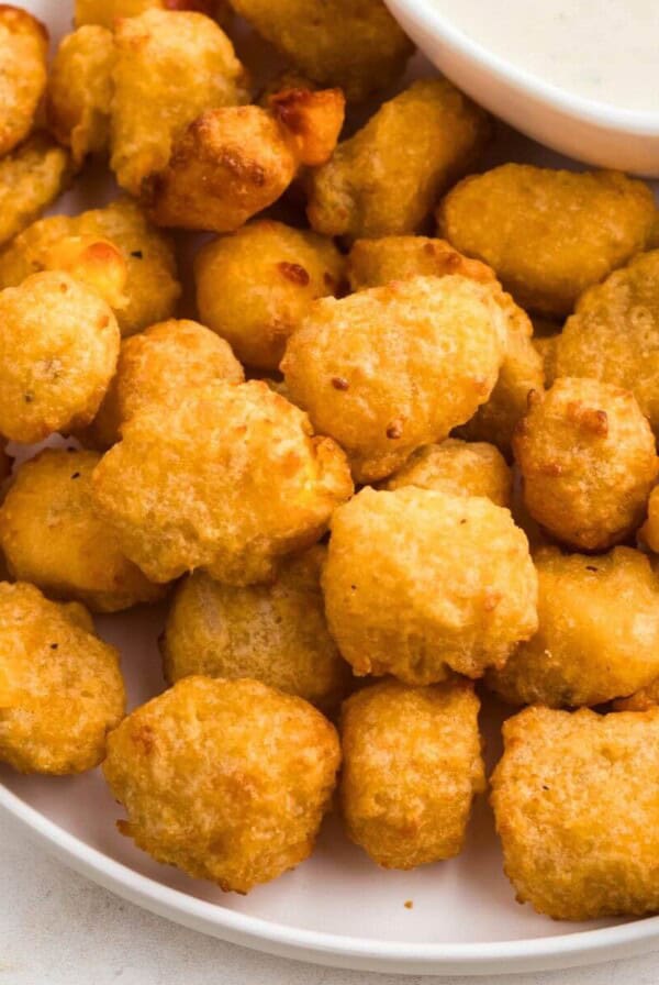 Golden brown breaded cheese curds stacked on a white plate with ranch dressing dip.