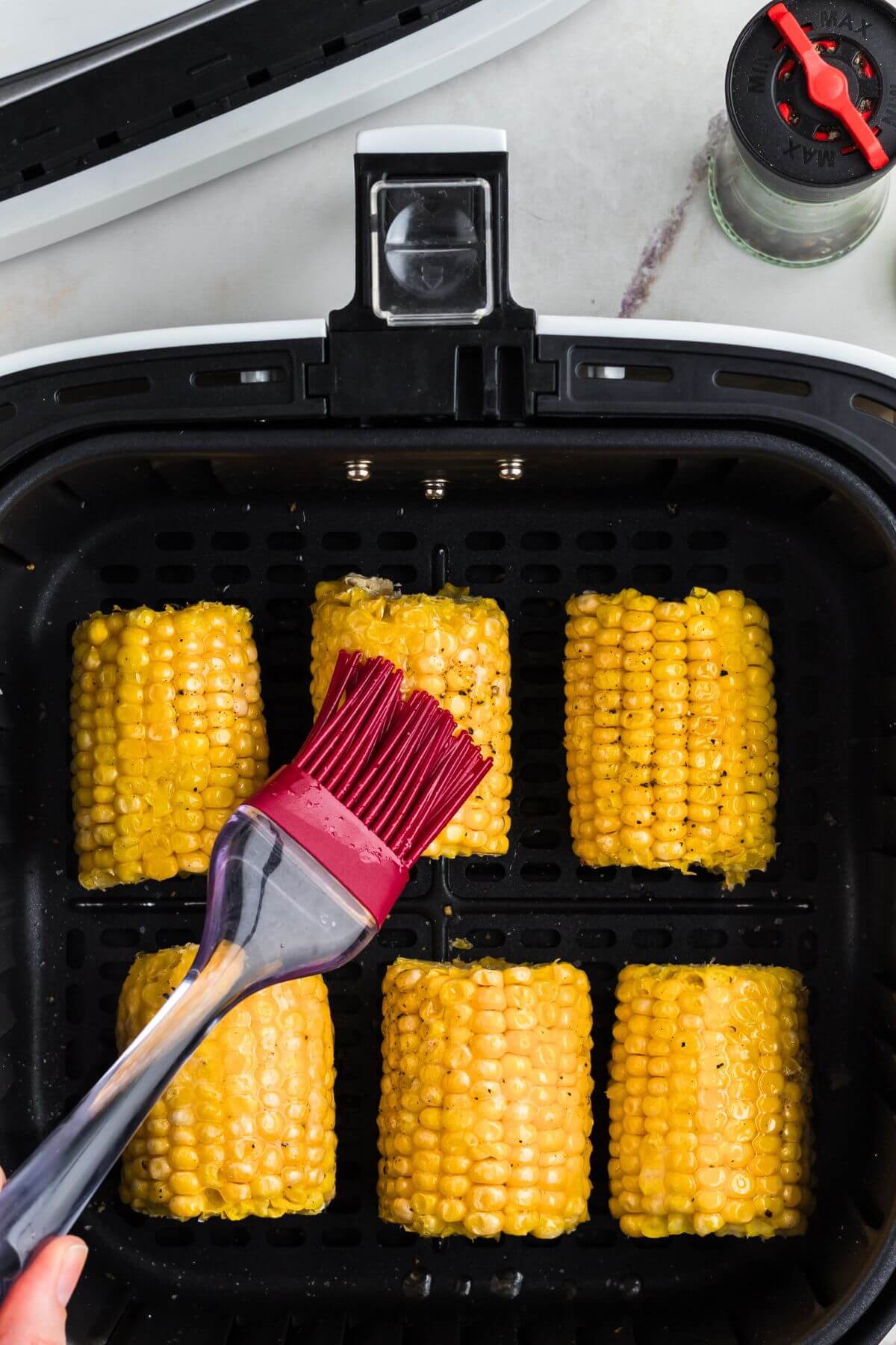 Brushing melted butter on corn along with salt and pepper. 