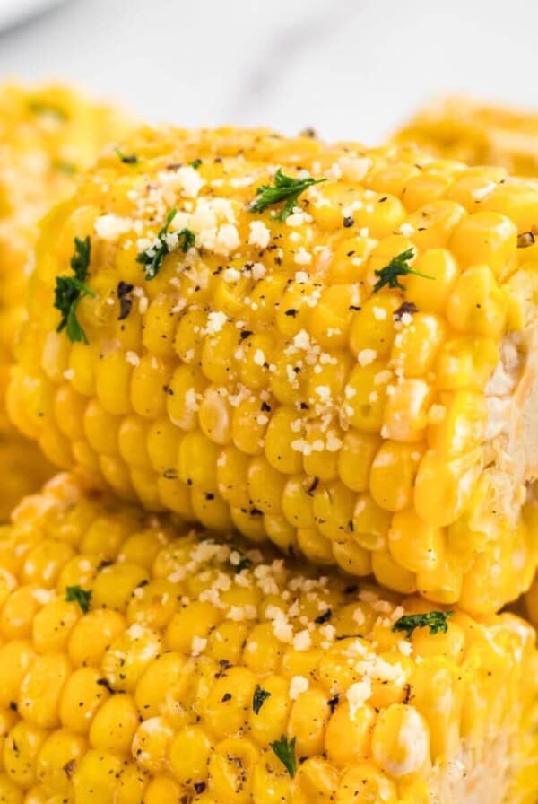 Golden yellow ears of corn stacked and garnished with parmesan cheese and parsley flakes.