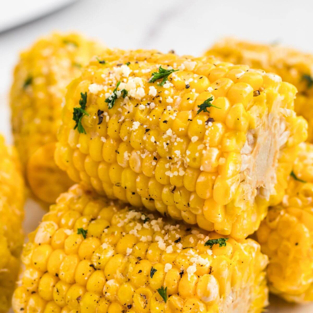 Golden yellow ears of corn stacked and garnished with parmesan cheese and parsley flakes.