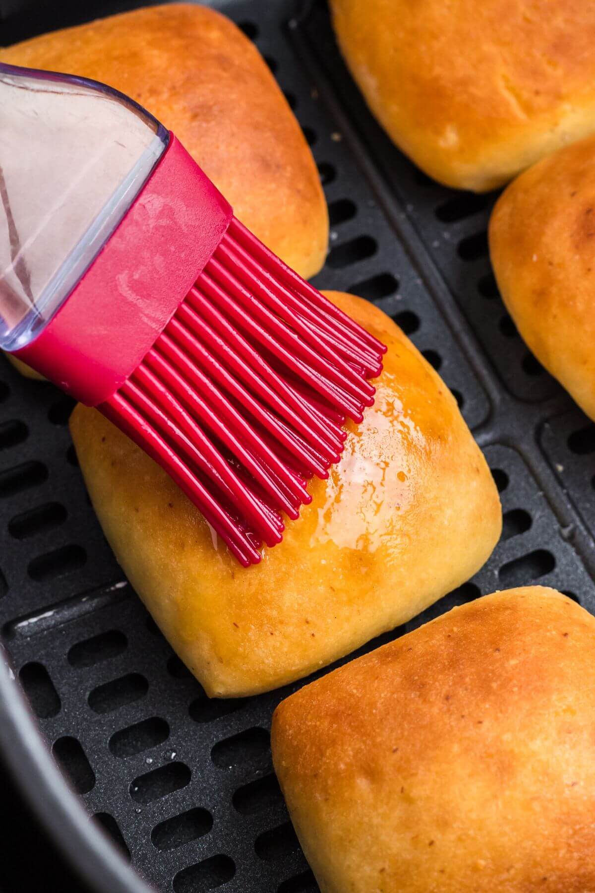 Melted butter being brushed onto dinner rolls in the air fryer basket. 