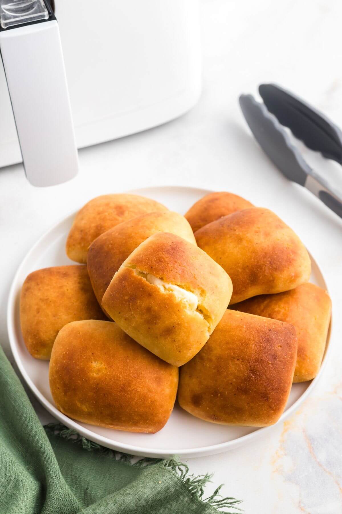 Golden soft dinner rolls stacked on a white plate with one sliced and buttered. 