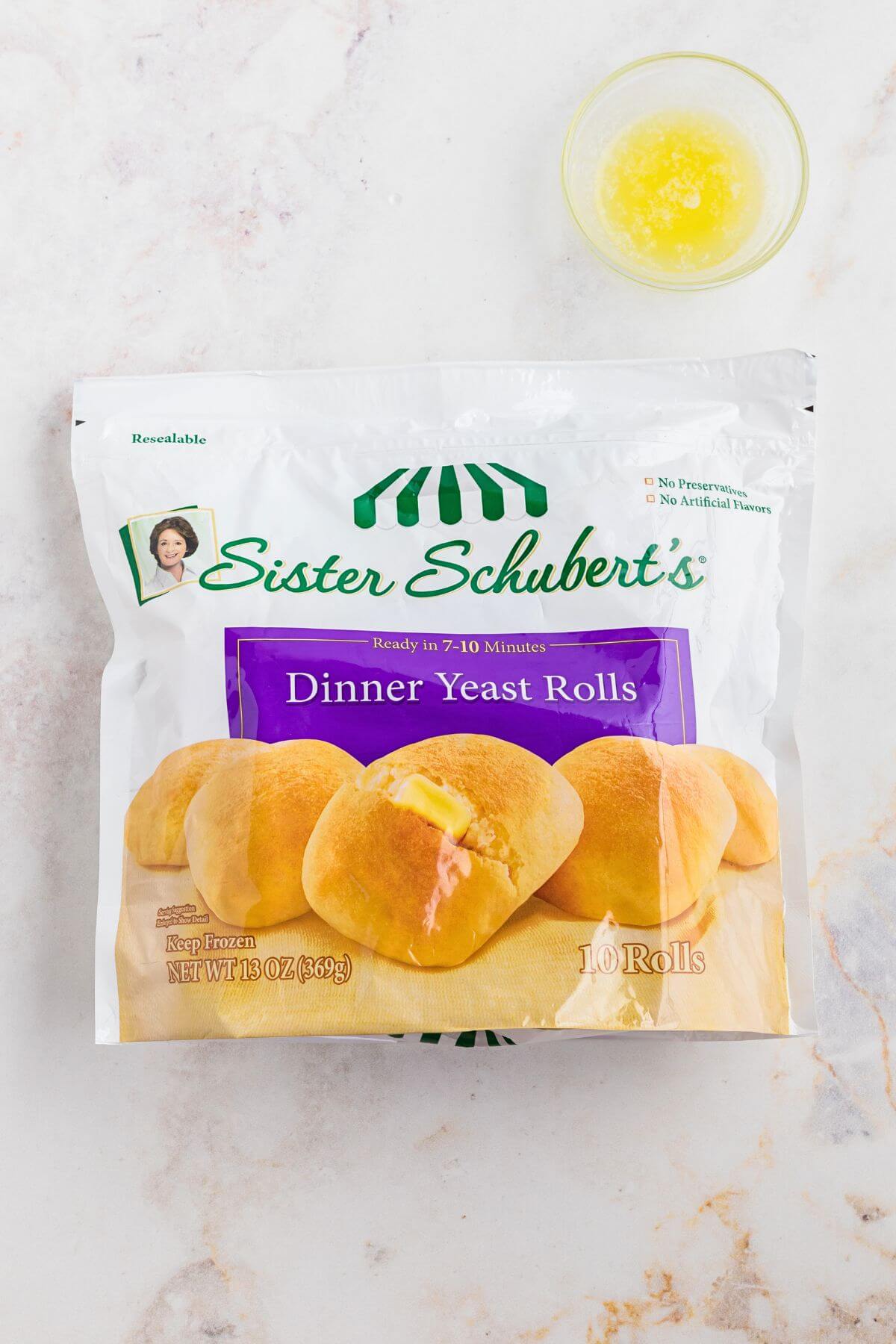 Package of Sister schuberts dinner yeast rolls on a marble table with a small bowl of melted butter. 