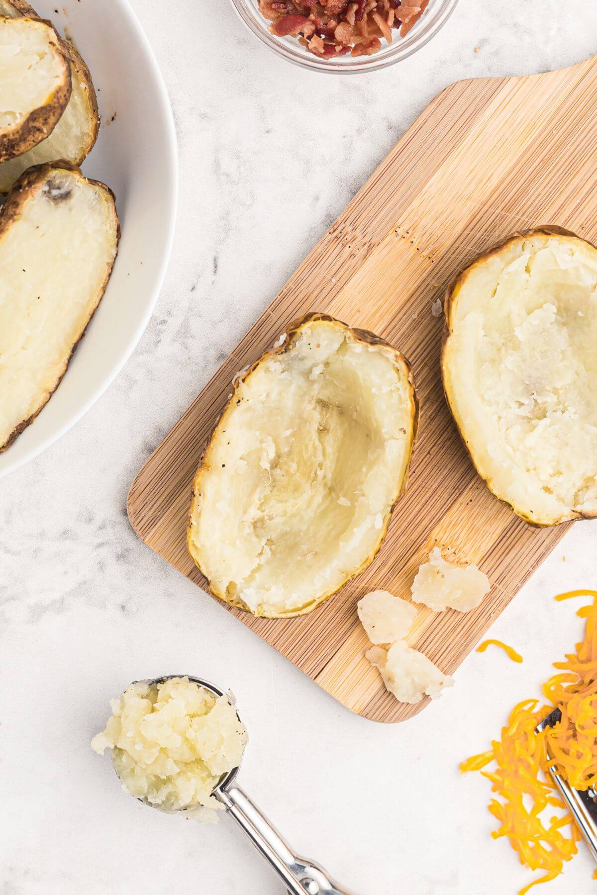 Baked potatoes sliced in half with centers scooped out on a cutting board. 