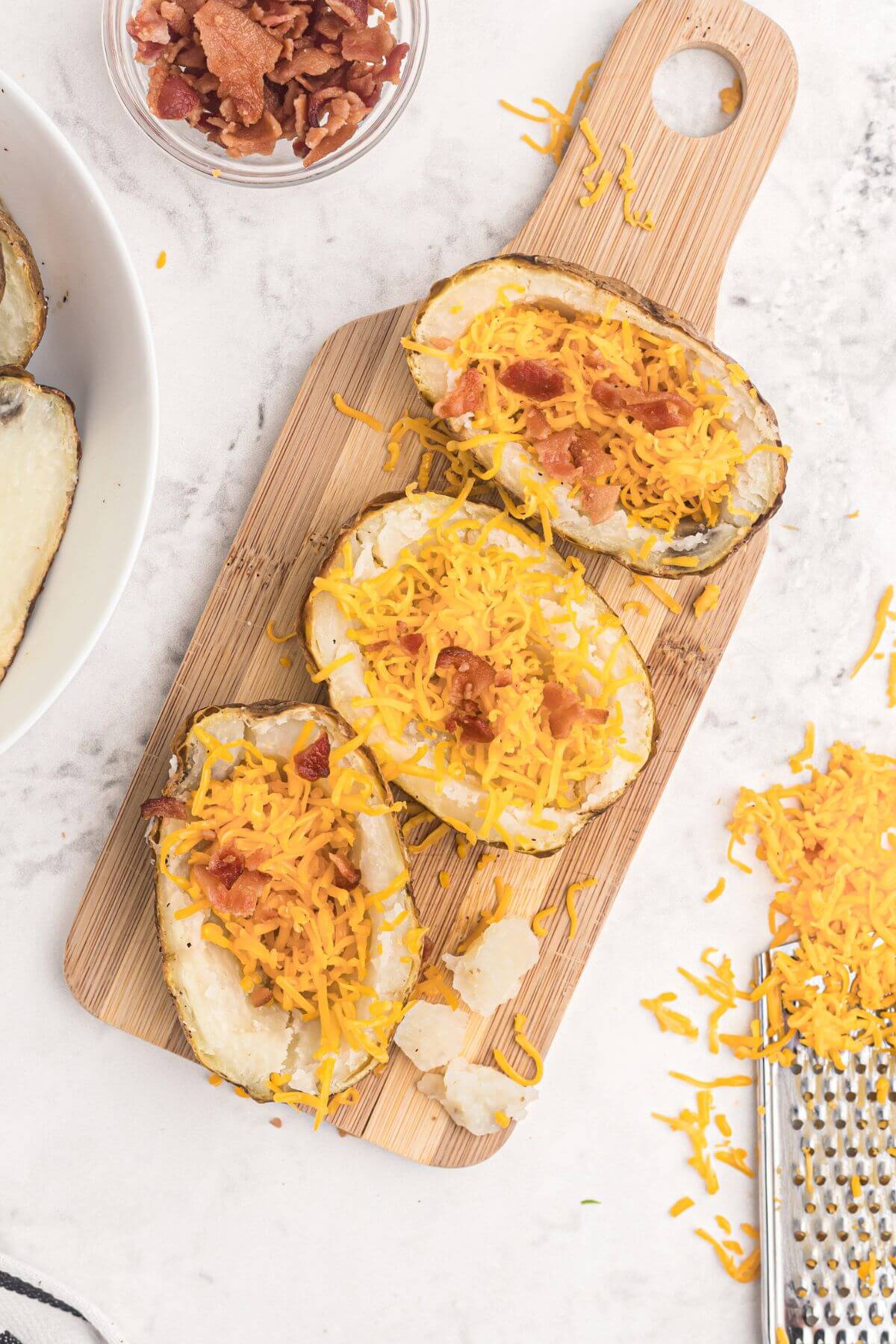 Baked potatoes scooped out then filled with shredded cheese and bacon crumbles. 