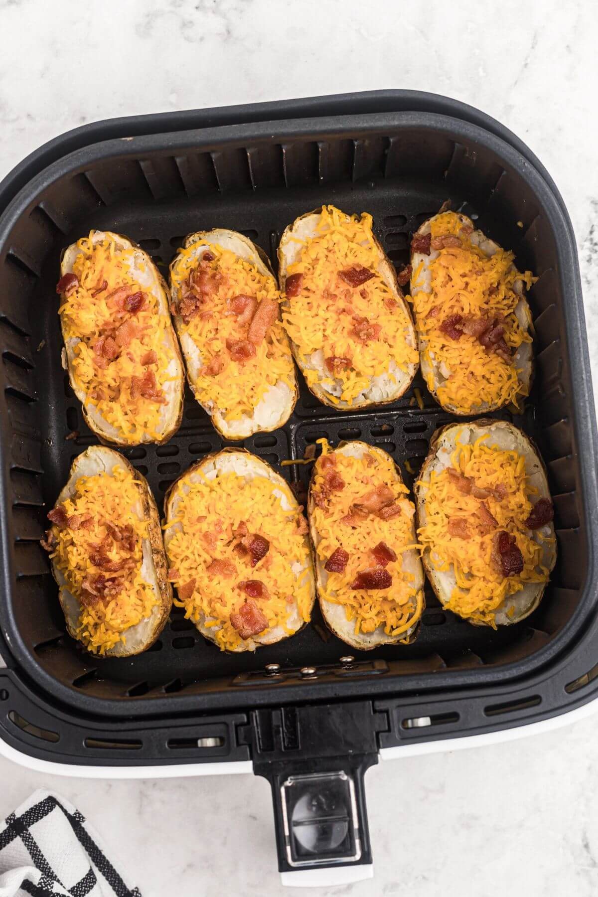 Baked potatoes stuffed with shredded cheese and chopped bacon, placed in the air fryer basket before being cooked. 