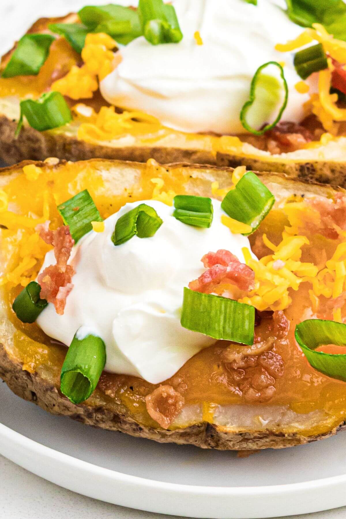 Close up photo of potato skin topped with cheese, bacon, sour cream and green onion. 