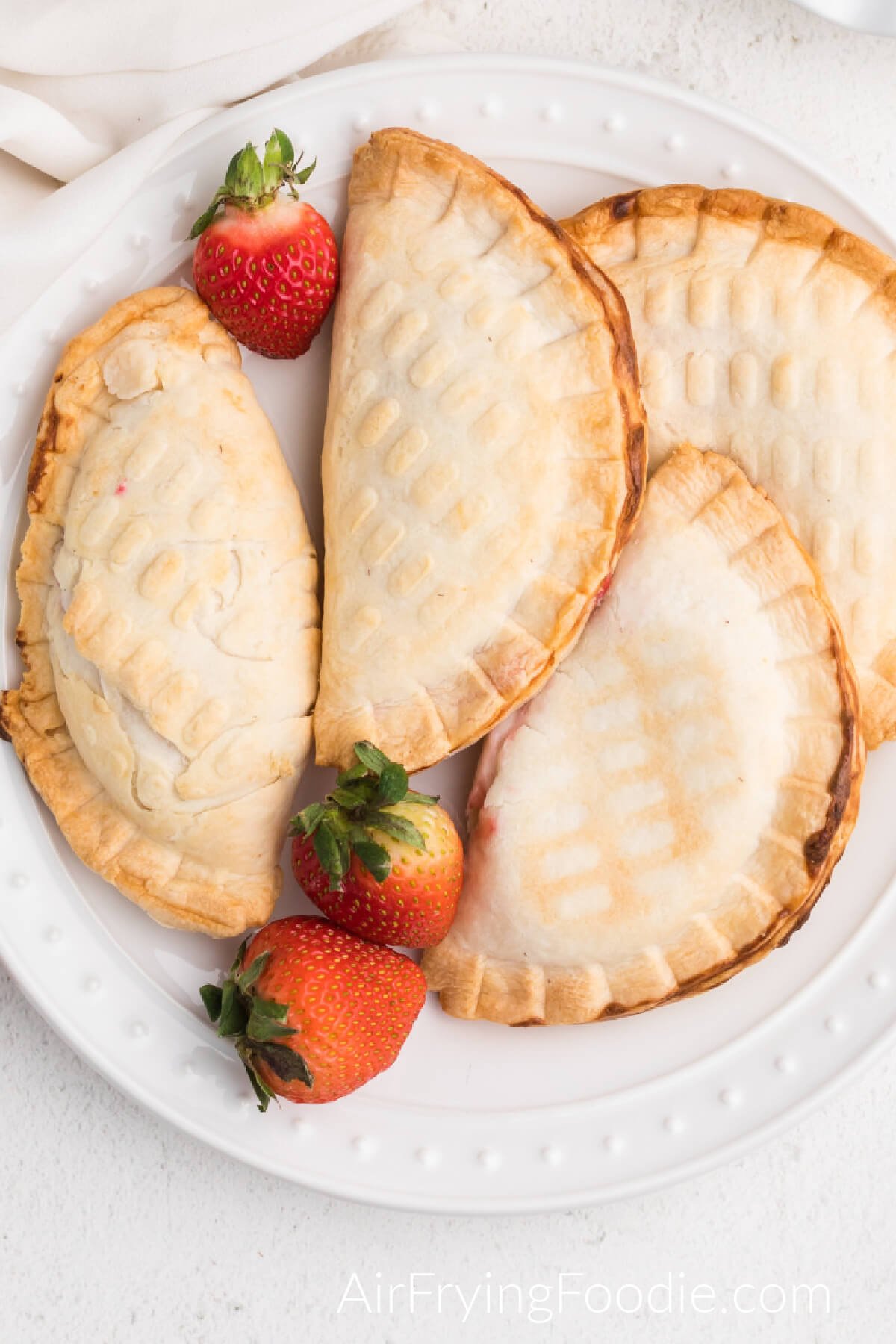 Air fried strawberry cream cheese hand pies on a white plate with fresh strawberries, ready to serve.