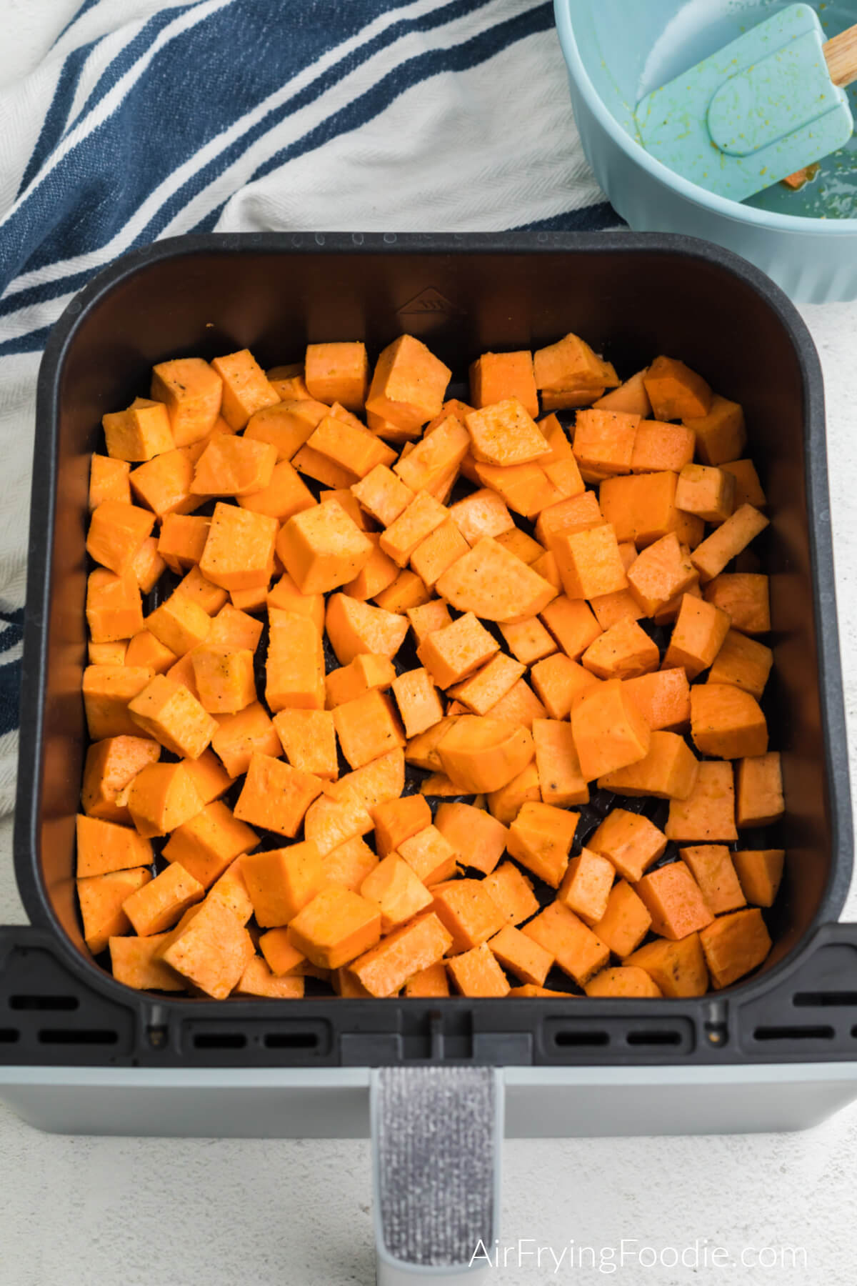 Oiled and seasoned sweet potato cubes in air fryer basket, ready to be cooked.