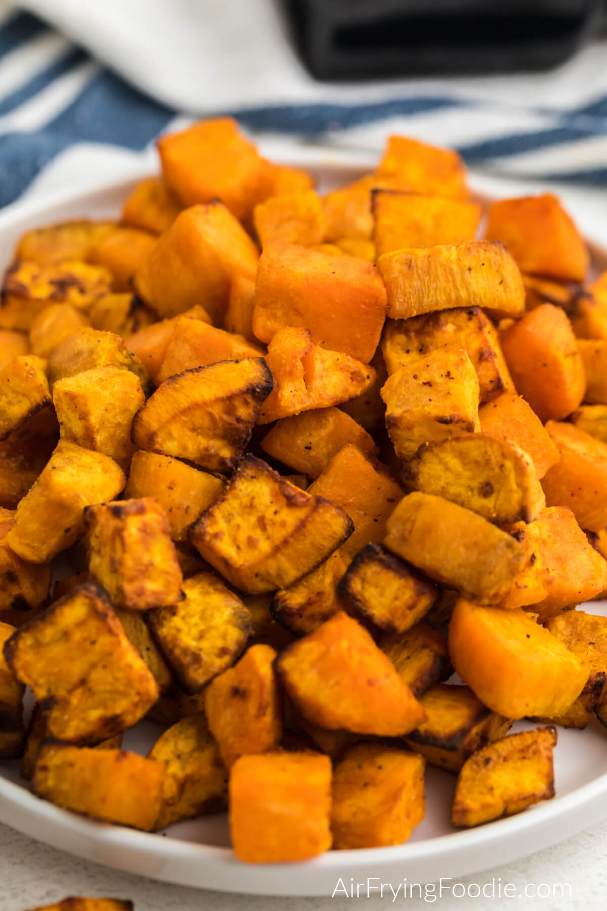 Close up photo of air fryer sweet potato cubes on a white plate, ready to eat. 