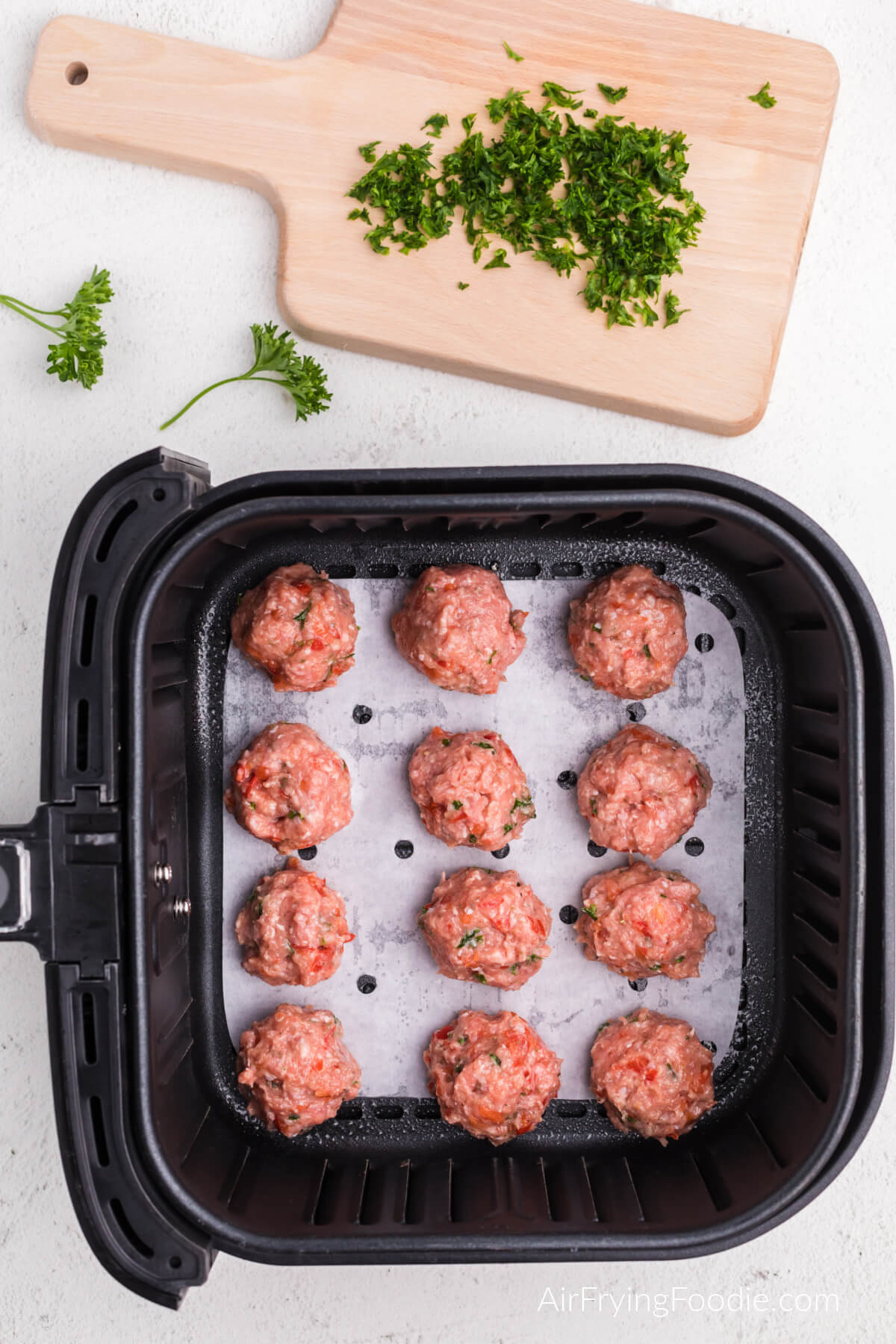 Turkey meatballs in the air fryer basket on a sheet of parchment paper. Ready to cook. 