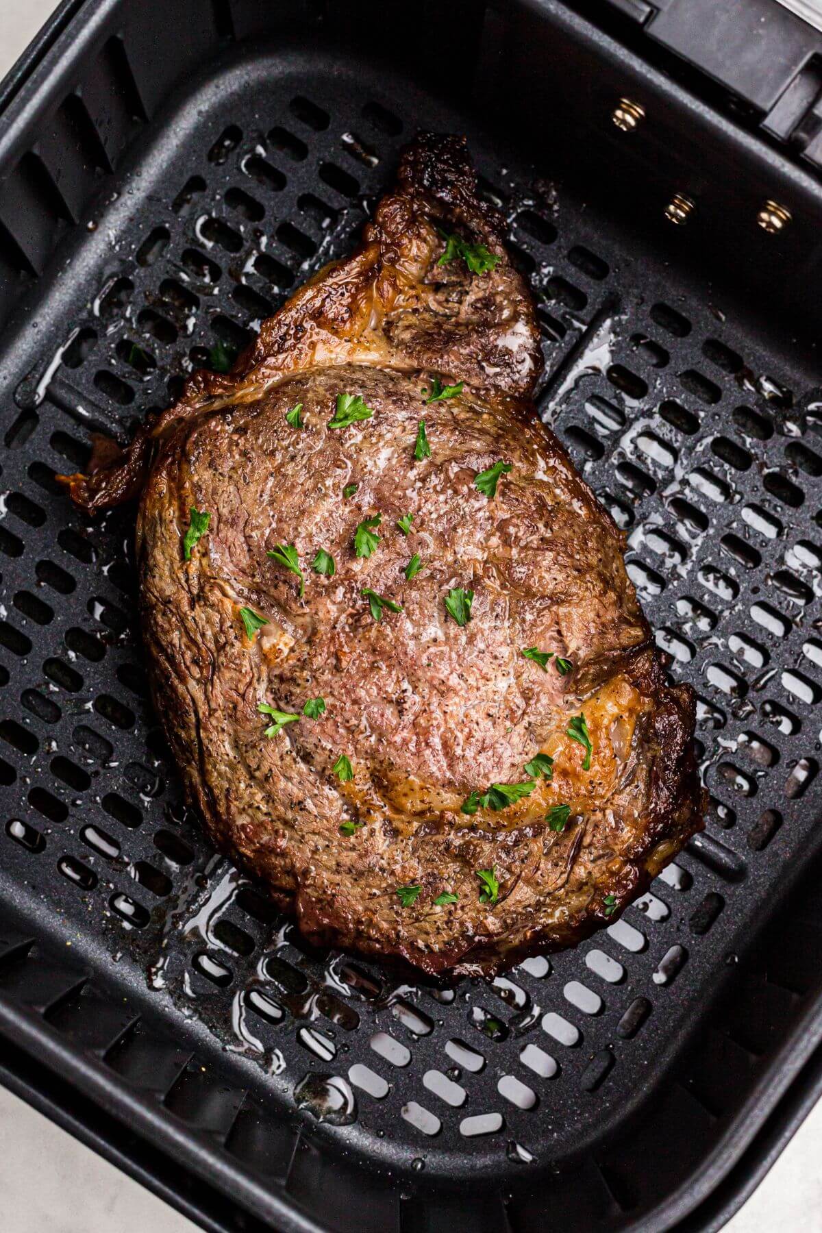 Juicy marbled steak in the air fryer basket garnished with parsley flakes. 