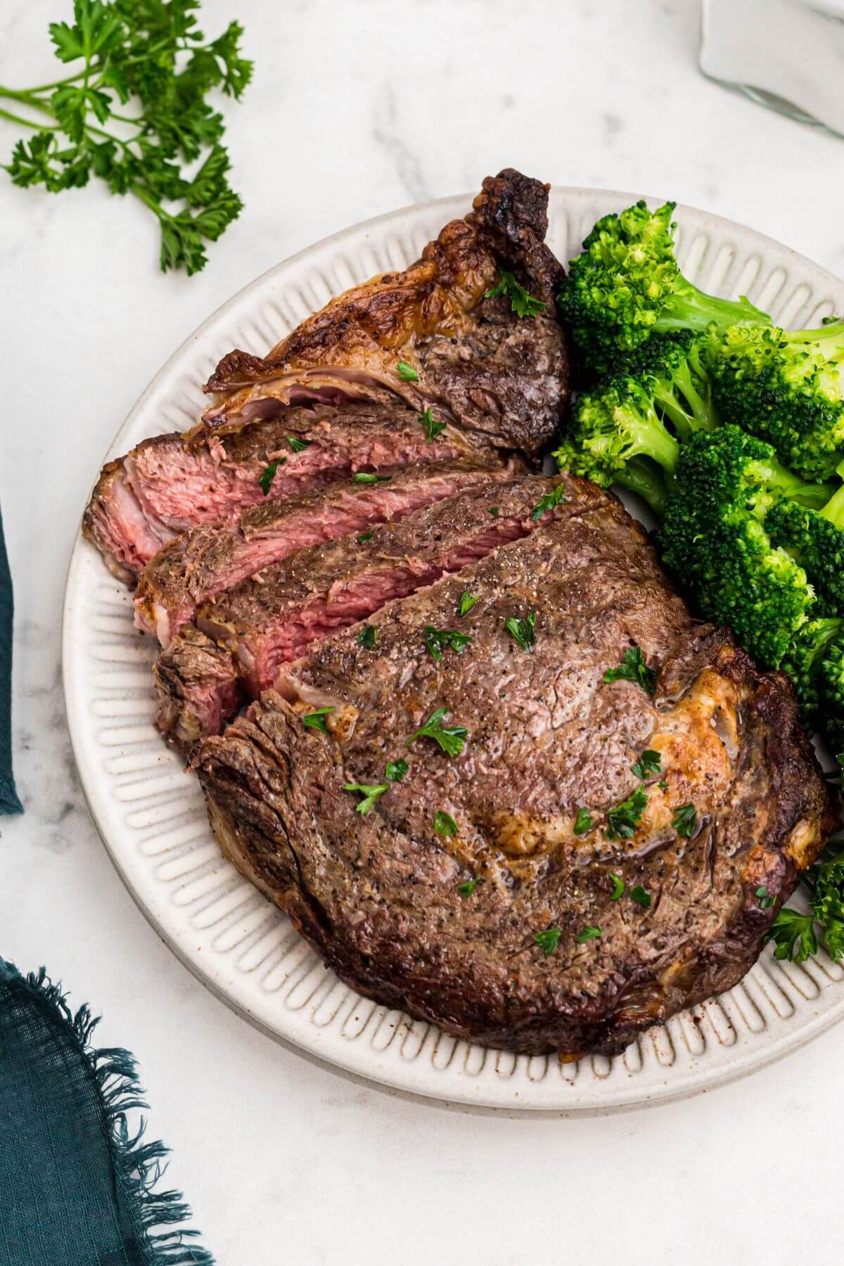 Juicy seasoned steak sliced and served with broccoli on a white plate. 