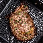 Juicy steak in the air fryer basket after being seasoned and cooked.
