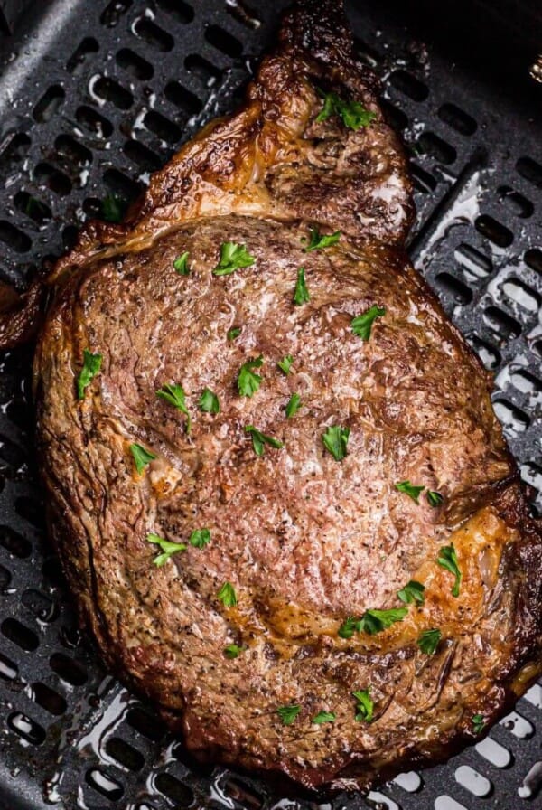 Juicy steak in the air fryer basket after being seasoned and cooked.