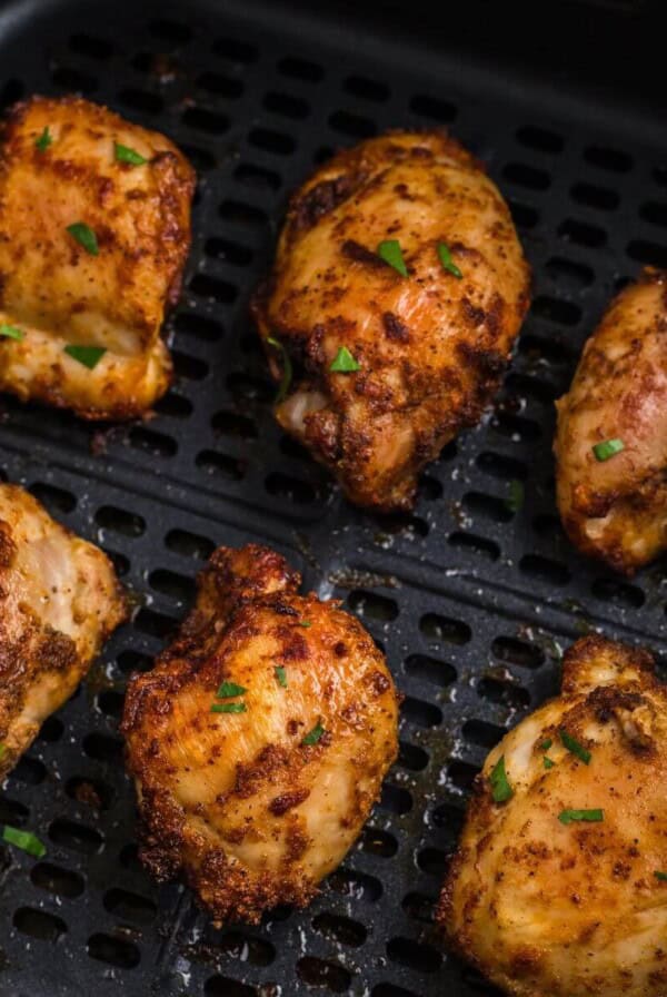 Crispy brown chicken thighs in the air fryer basket.