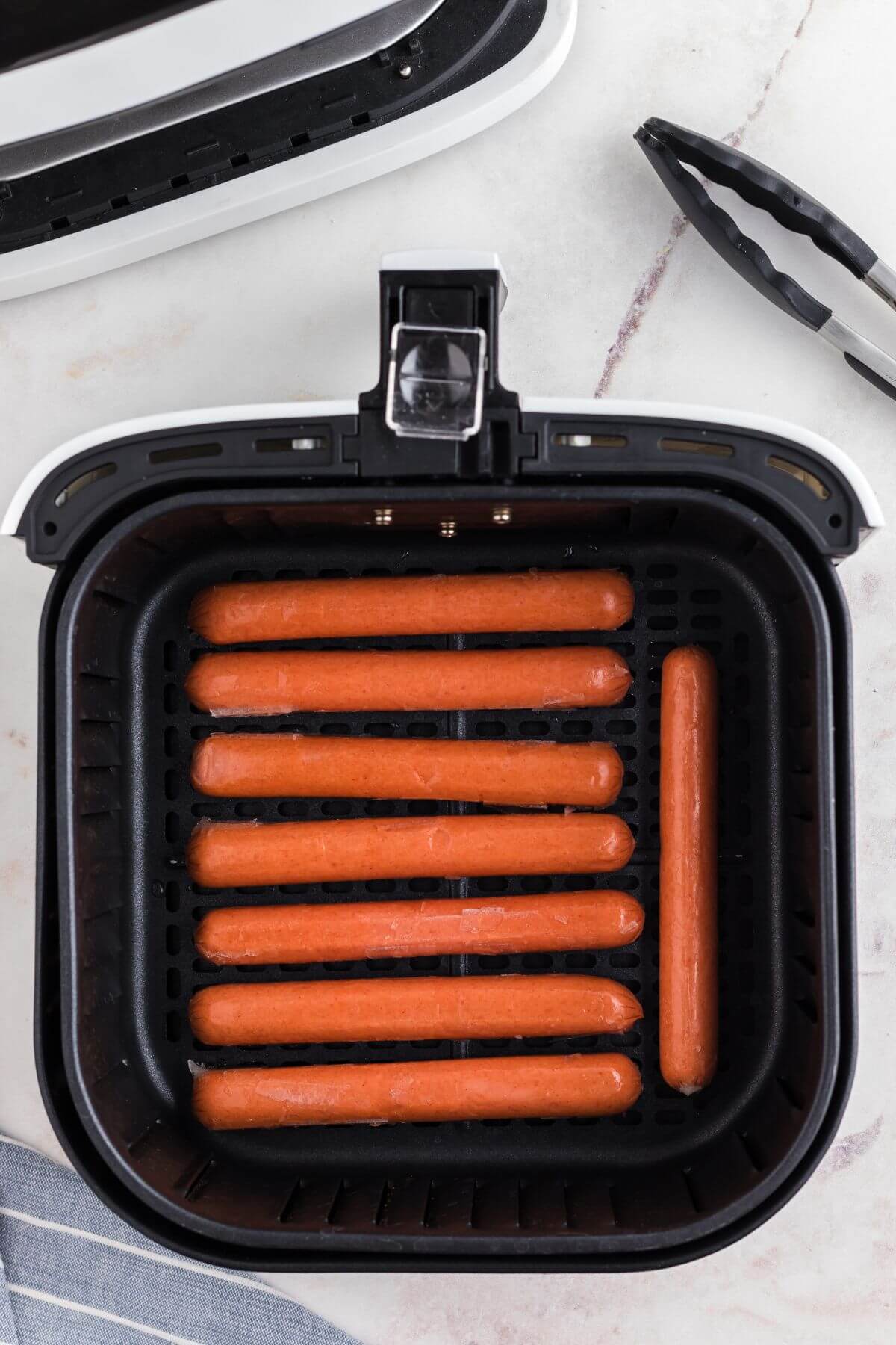 Uncooked frozen hot dogs in the air fryer basked before being cooked. 