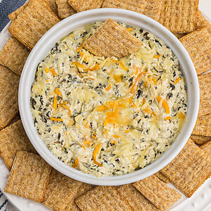 Air fryer artichoke spinach dip in a dish surrounded by Triscuit chips for dipping.