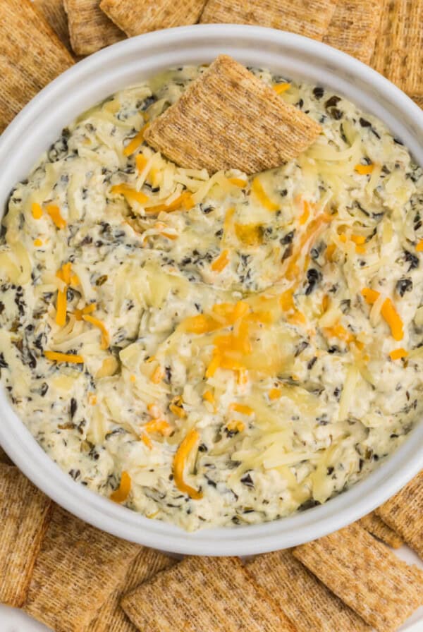 Air fryer artichoke spinach dip in a dish surrounded by Triscuit chips for dipping.