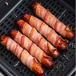 Juicy and crispy bacon wrapped hot dogs in the air fryer basket after being cooked.