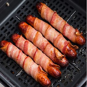 Juicy and crispy bacon wrapped hot dogs in the air fryer basket after being cooked.