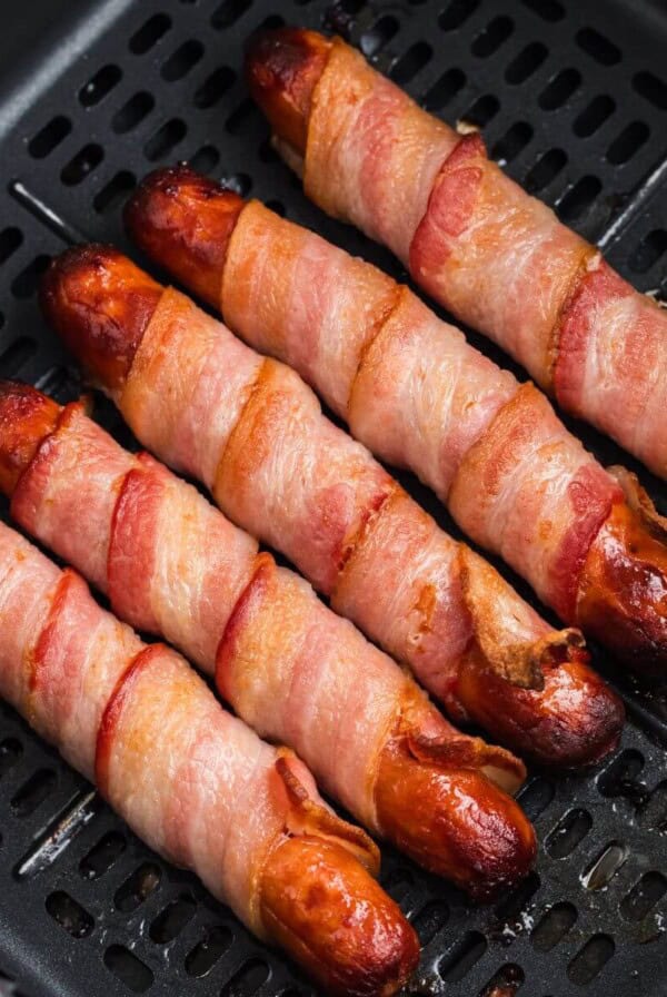 Juicy and crispy bacon wrapped hot dogs in the air fryer basket after being cooked.