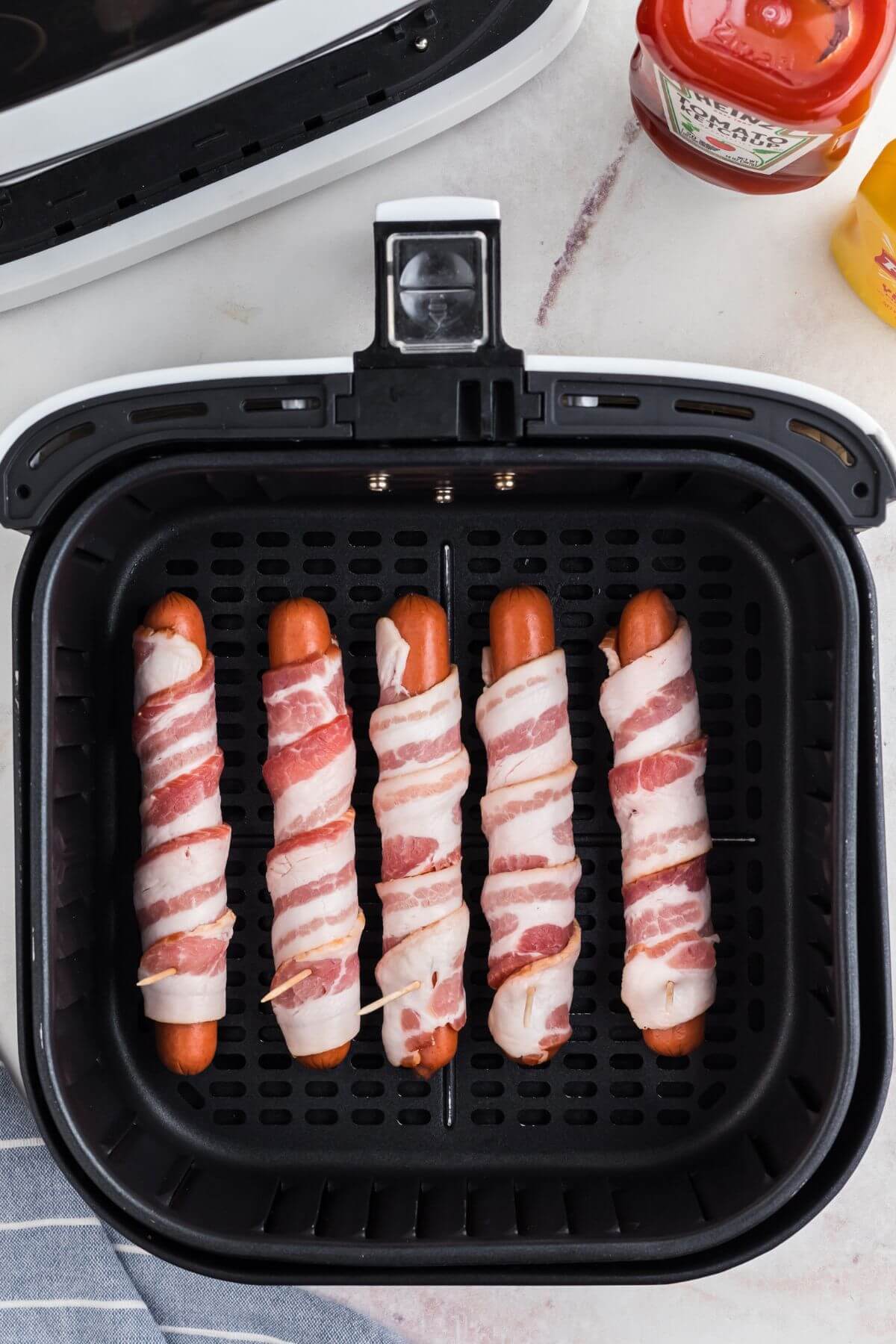 Hot dog wrapped in uncooked bacon in the air fryer basket. 
